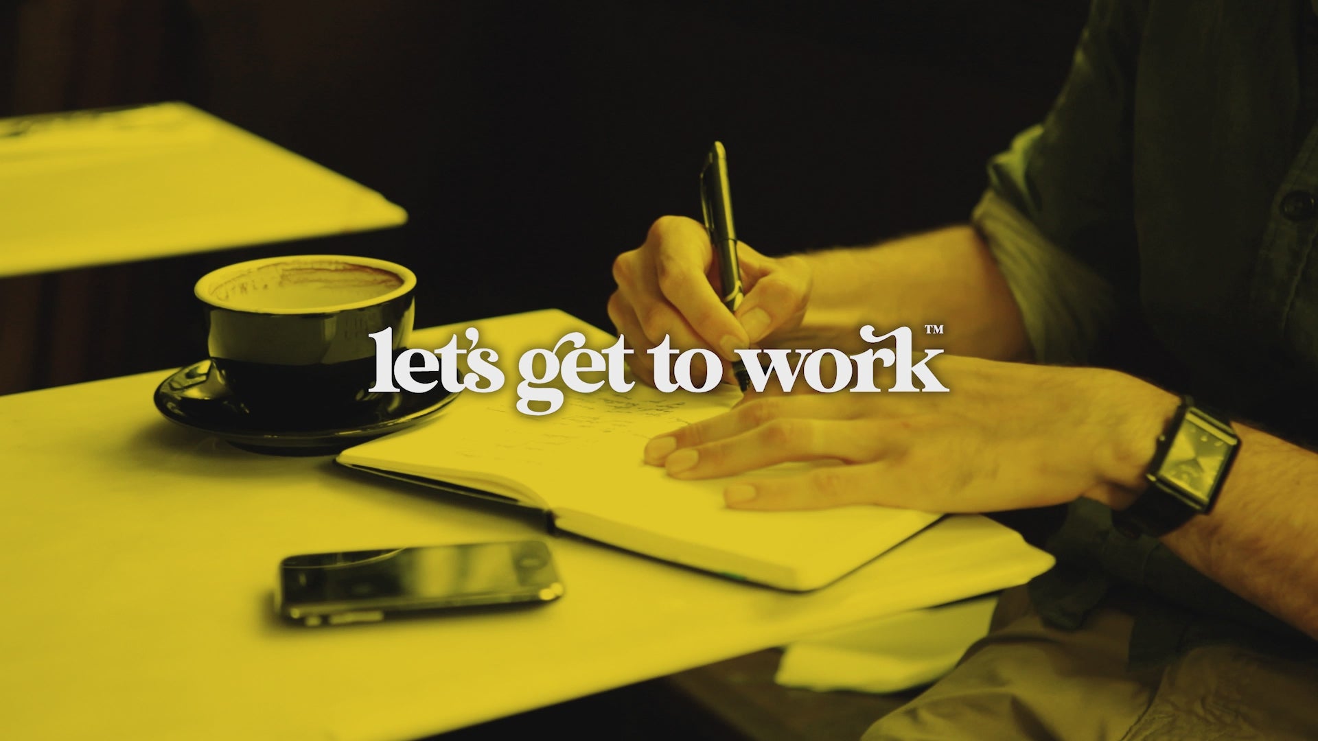 A man making journal notes in a coffee shop with the words "let's get to work" floating over the top